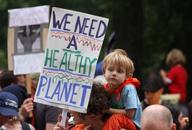 Child on father's shoulders with sign reading "We need a healthy planet"